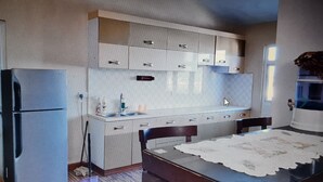 Cocina pequeña con refrigerador, pileta y alacenas. Posee una cama con cabecera de madera y una ventana con persianas.