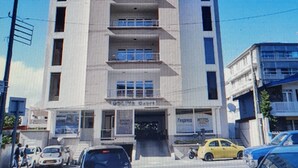 Un edificio de varios pisos con una entrada central, varias ventanas en cada nivel y algunos coches aparcados en la parte delantera.
