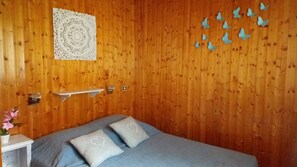 A wooden-paneled room with a bed, a small table with a potted plant, a wall hanging, and butterfly decorations.