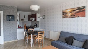Un salon moderne avec un canapé bleu, une table à manger avec des chaises et un coin cuisine doté de placards et d’un luminaire suspendu.