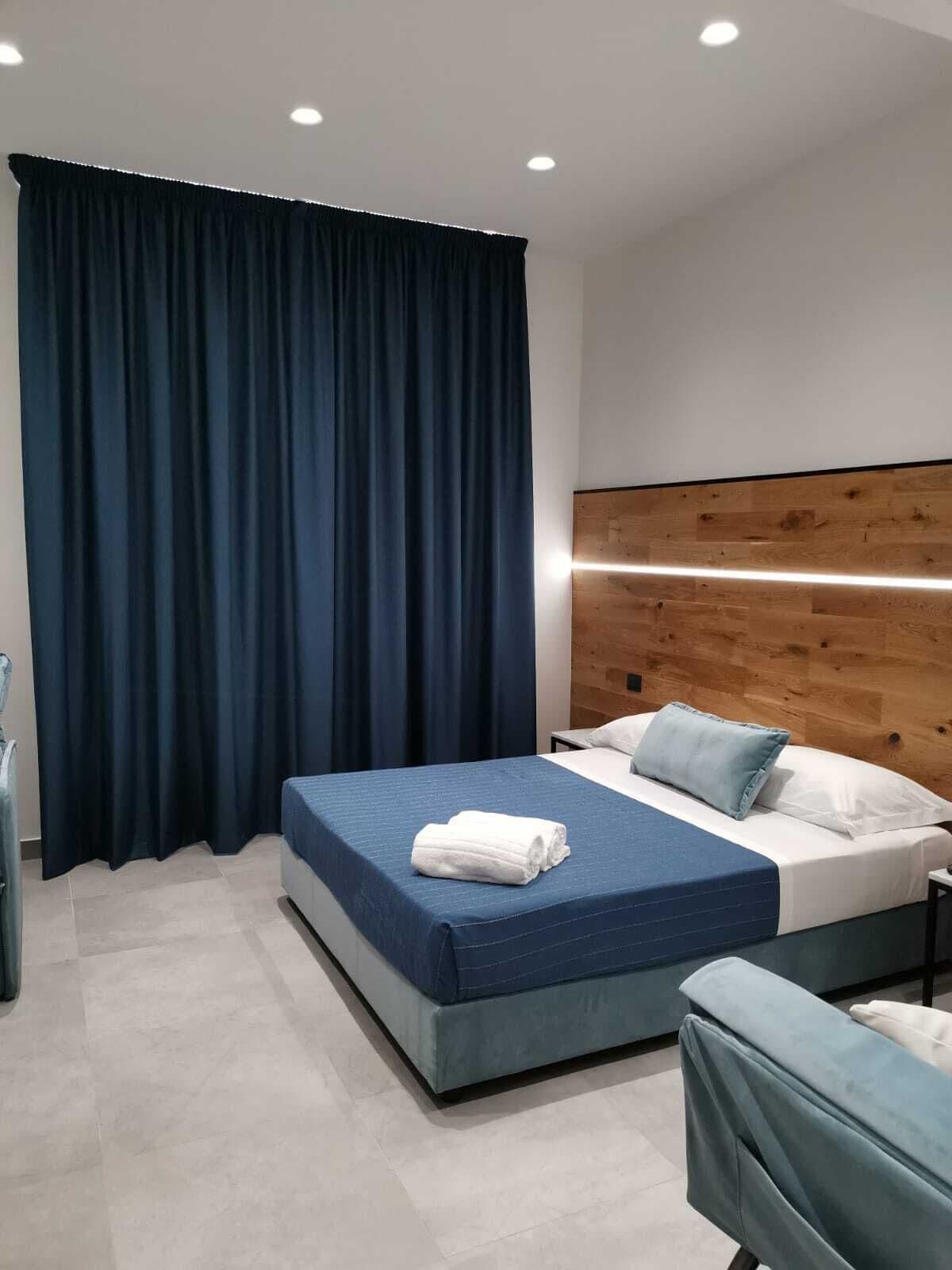 Une chambre d’hôtel moderne avec un grand lit, une tête de lit en bois et des rideaux foncés.