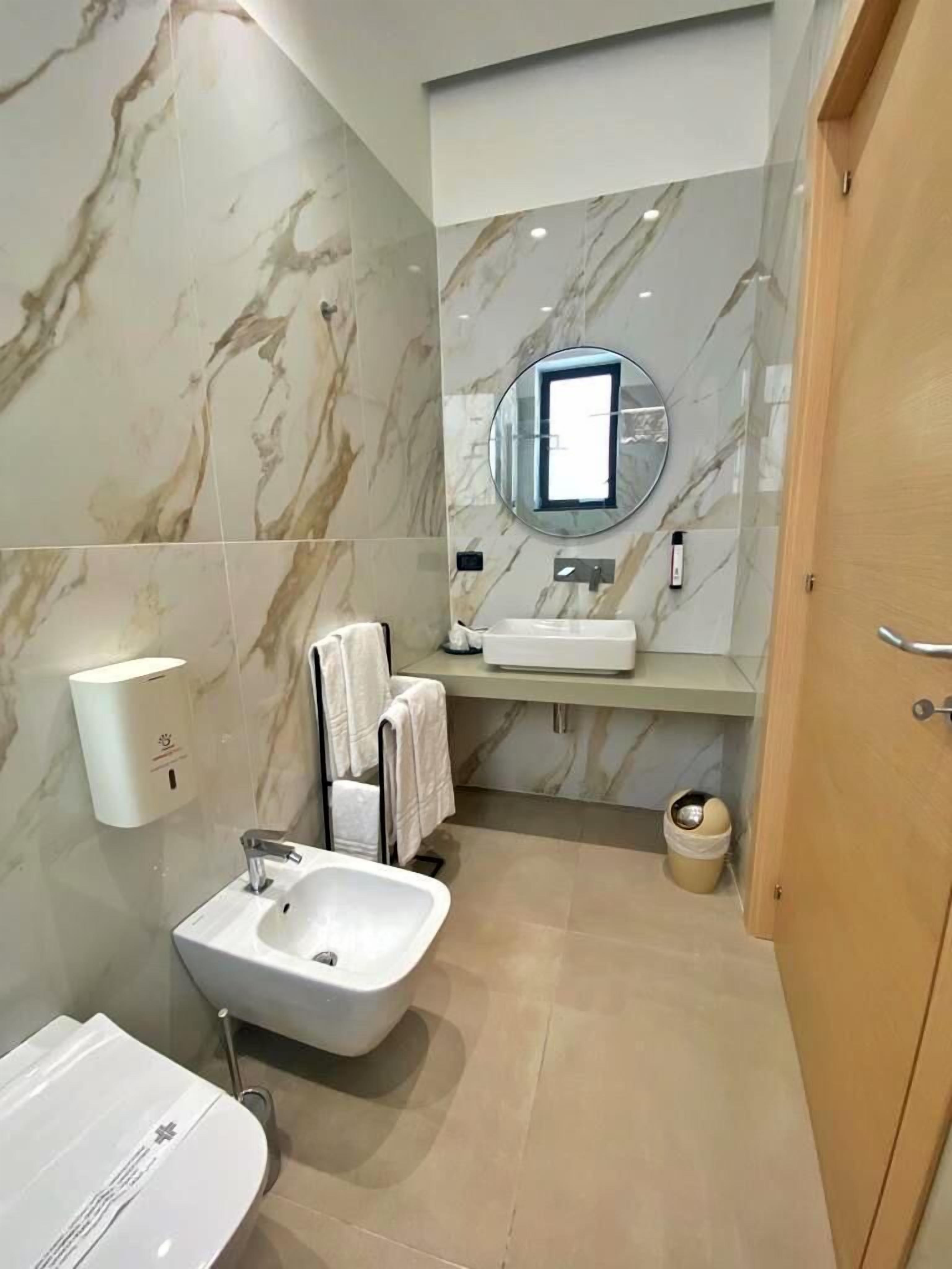 Une salle de bain moderne avec un mur en marbre, un lavabo, un miroir, un porte-serviettes et des toilettes.