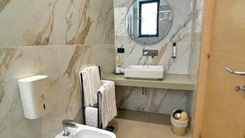 Un baño moderno con pared de mármol, un lavamanos, un espejo, un perchero para toallas y un inodoro.