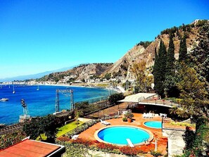 A coastal resort with two swimming pools, a beach, and a mountainous backdrop.