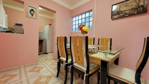 A dining area with a table and chairs, a window with a view, and a kitchen in the background.