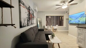 A modern living room with a grey sofa, a white coffee table, and a TV mounted on the wall. - Barefoot Mailman Inn & Suites (Lantana)
