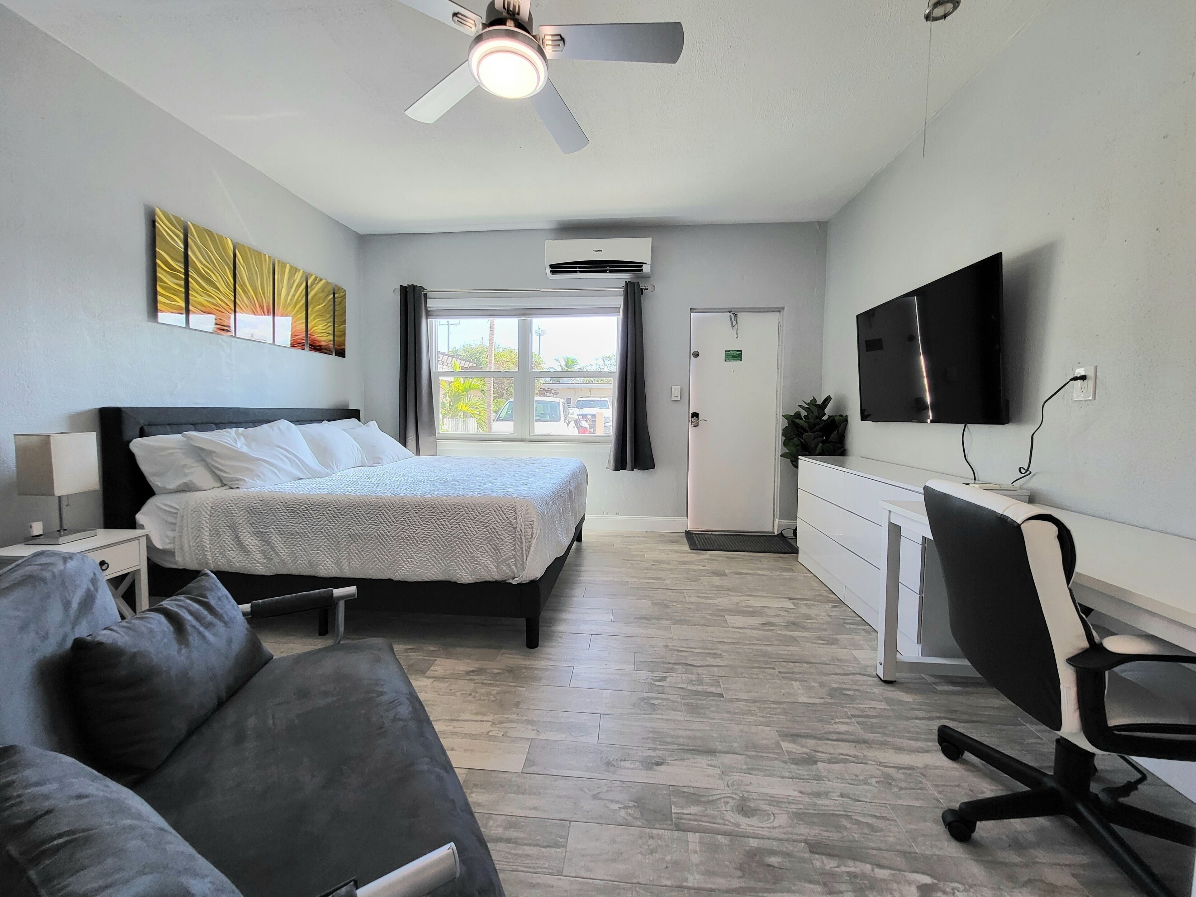 A hotel room with a bed, a desk, a chair, a TV, and a ceiling fan.