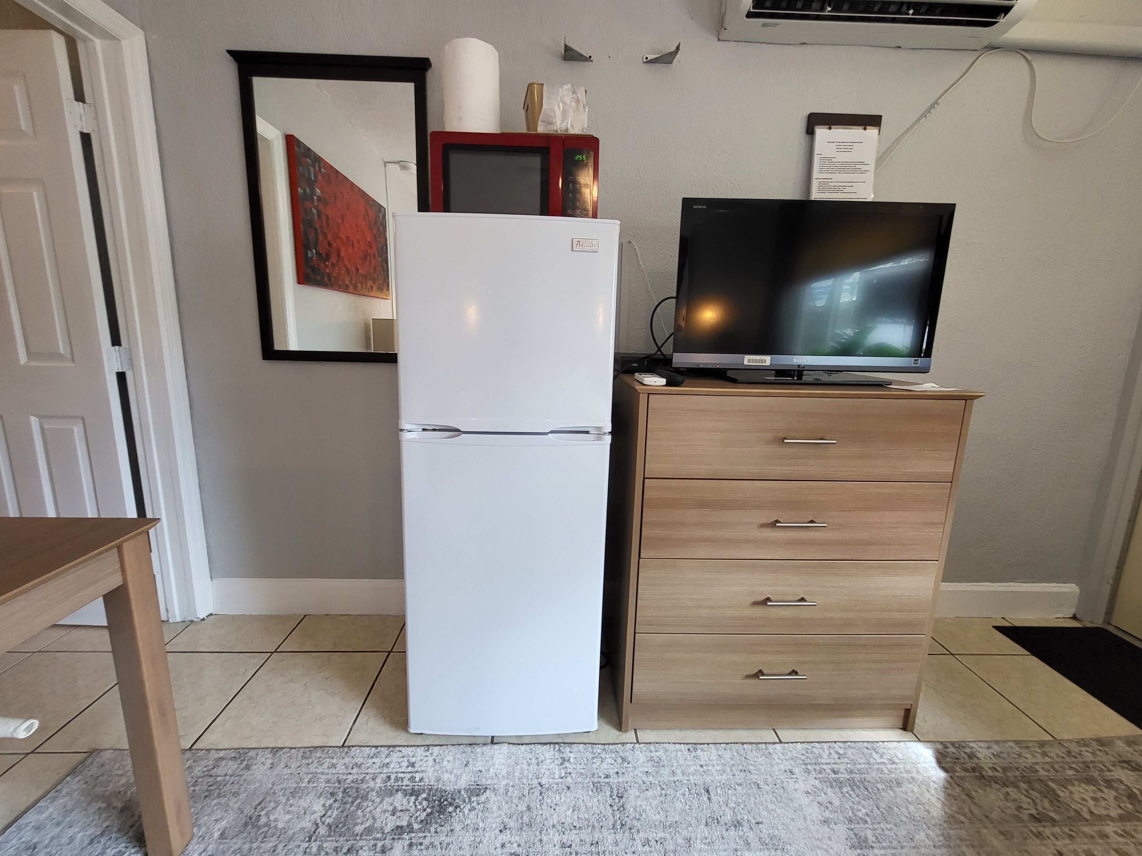 Une cuisine de taille réduite avec un réfrigérateur blanc, un meuble en bois intégrant un téléviseur à écran plat et un sol carrelé.