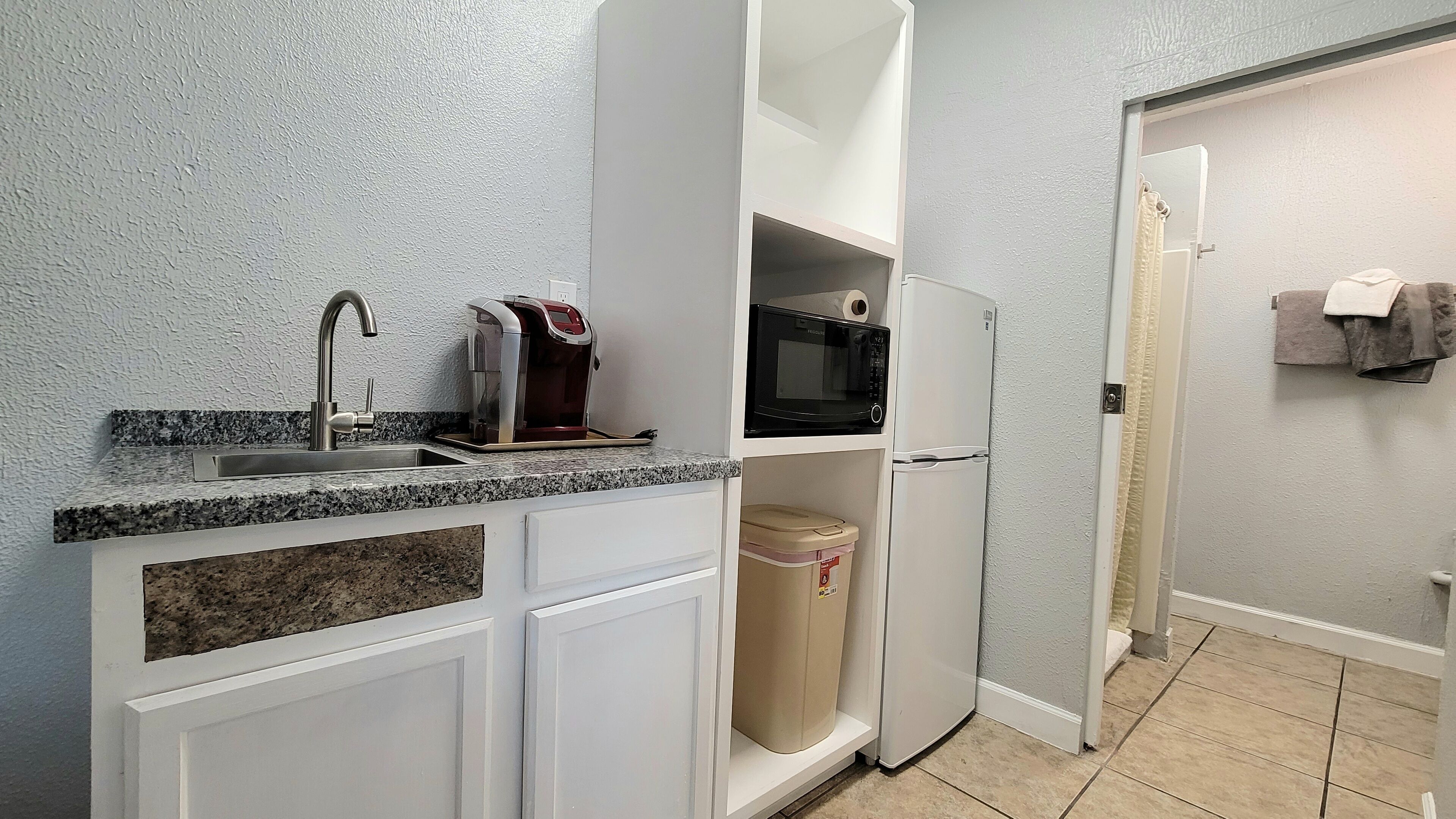 Uma cozinha compacta com bancada de granito, pia de aço inoxidável, cafeteira, micro-ondas e geladeira.