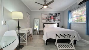 A modern bedroom with a bed, desk, chair, and a ceiling fan. - Barefoot Mailman Inn & Suites (Lantana)