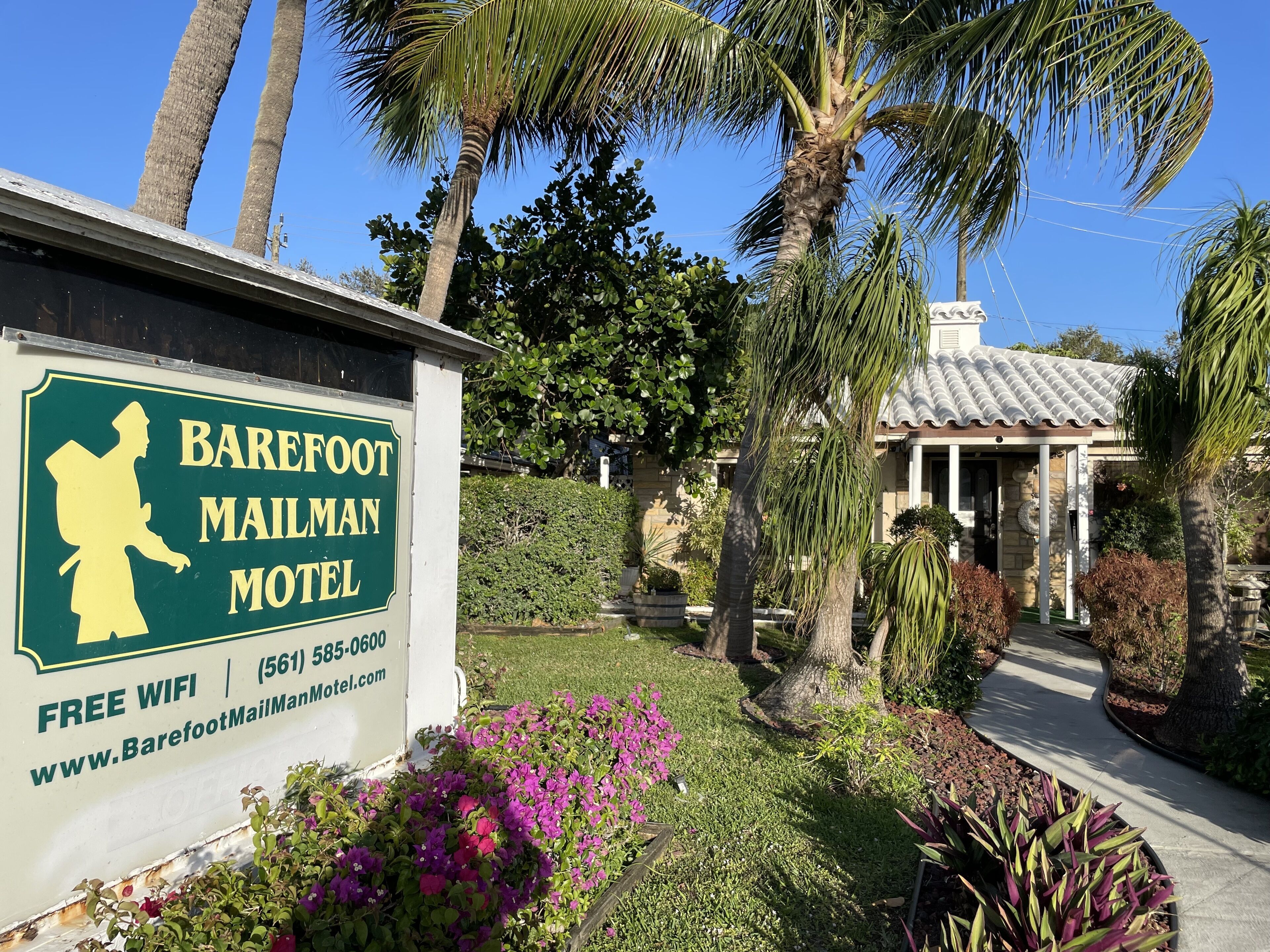 A sign for Barefoot Mailman Motel with a silhouette of a mailman, free WiFi, and a website URL.