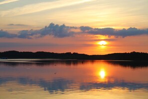 Un coucher de soleil sur un lac paisible, avec la silhouette d’arbres en arrière-plan.