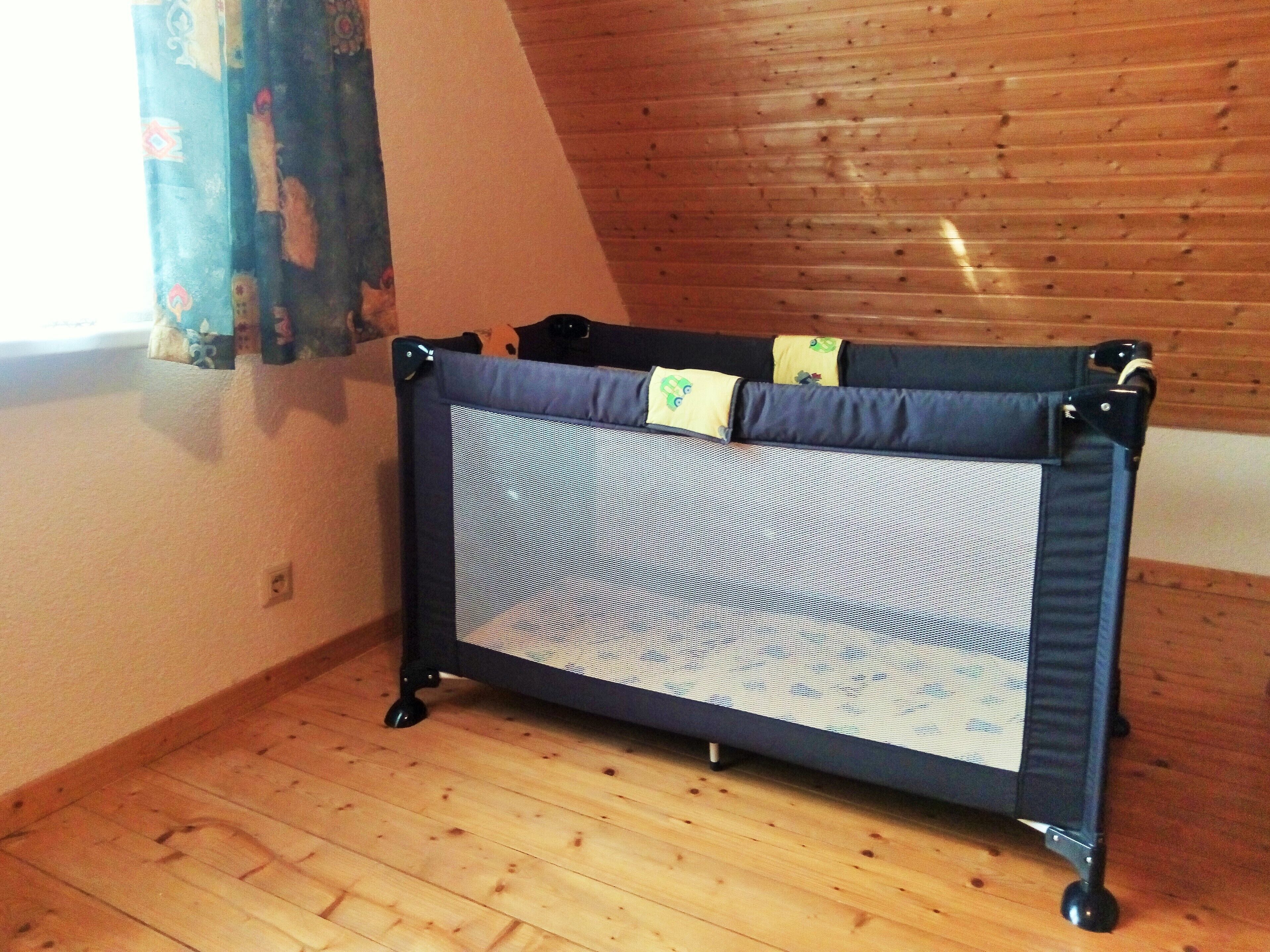 Une pièce avec un plancher en bois, une fenêtre avec des rideaux et une barrière de sécurité pour bébé munie d’un grillage.