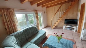 A living room with a sofa, a table with a vase of flowers, a TV, and a wooden staircase.