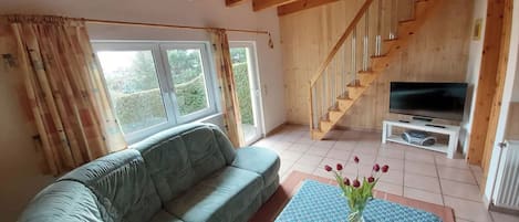 A living room with a sofa, a table with a vase of flowers, a TV, and a wooden staircase.