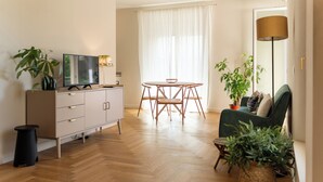 Een moderne woonkamer met houten vloer, een eettafel met stoelen, een bank, een televisie en verschillende potplanten.