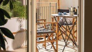 Een open deur leidt naar een balkon met een tafel, stoelen en een hanglamp.