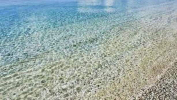 Een heldere blauwe zee met een kiezelstrand en verafgelegen bergen.