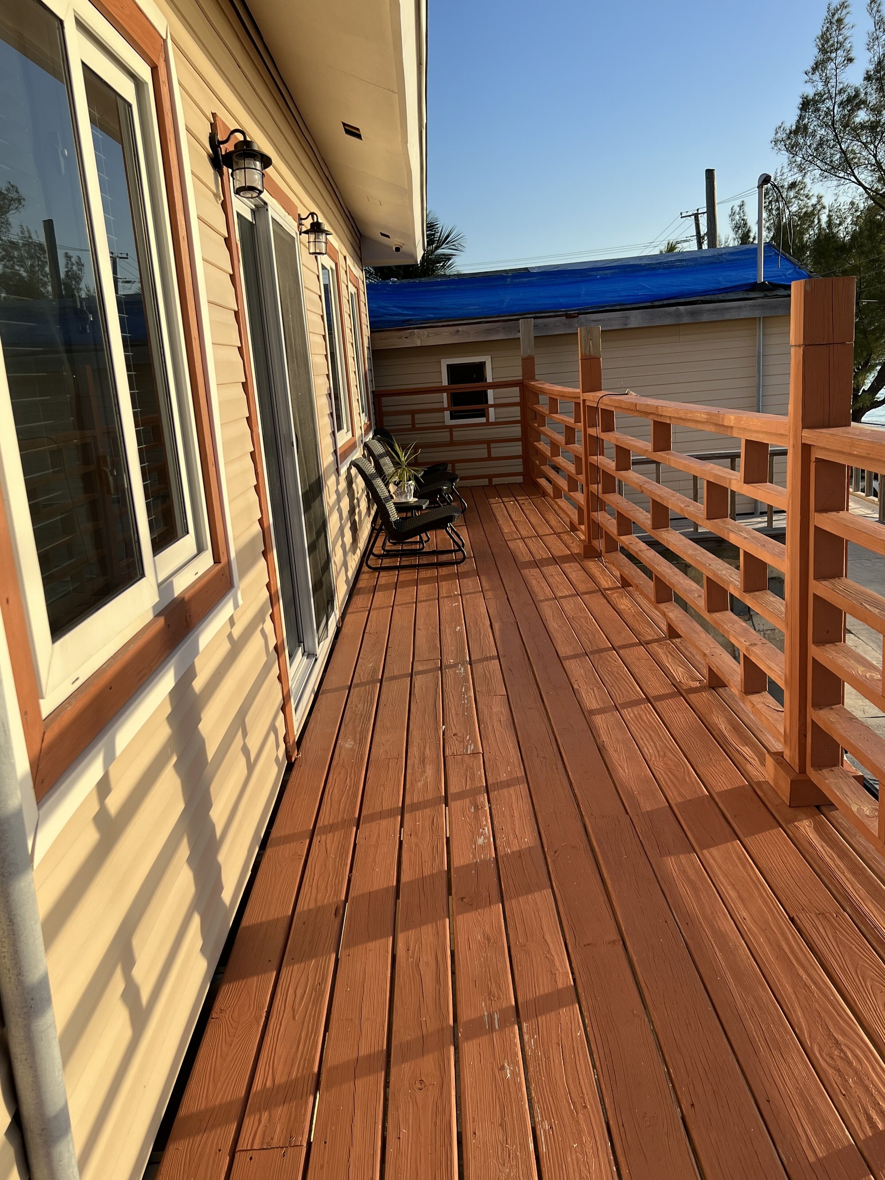A wooden deck with a railing, a table with chairs, and a potted plant.