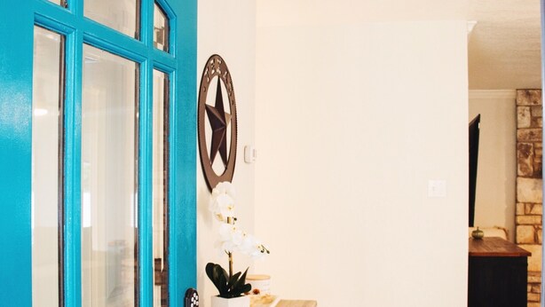 Een blauwgroene deur met glaspanelen, een decoratie in de vorm van een ster, een houten dressoir en een stenen muur op de achtergrond.