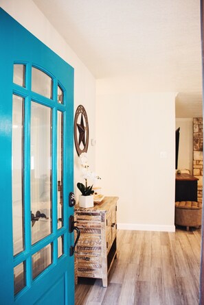 A teal door with glass panels, a star-shaped wall decoration, a wooden chest of drawers, and a stone wall in the background.