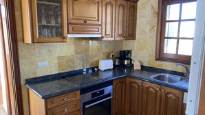 A kitchen with wooden cabinets, a marble backsplash, a toaster, a coffee maker, and a dishwasher. - Casa Sophia (Playa Blanca)