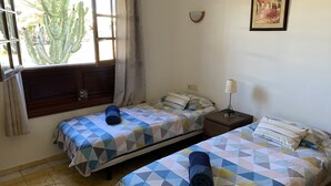 A room with two beds, a nightstand, a lamp, and a window with curtains. - Casa Sophia (Playa Blanca)