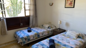 A room with two beds, a nightstand, a lamp, and a window with curtains.