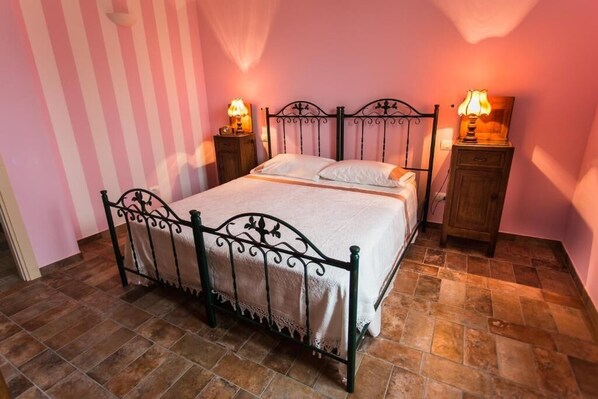 A single bed with a metal frame, two bedside tables with lamps, and a pink-striped wall.