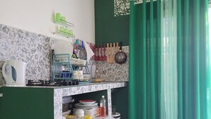 A kitchen with a gas stove, a sink, and a countertop with various kitchen items. There is a patterned backsplash and a green curtain.