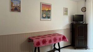 Una habitación con una mesa cubierta por un mantel a cuadros, un televisor sobre un mueble y tres cuadros enmarcados en la pared.