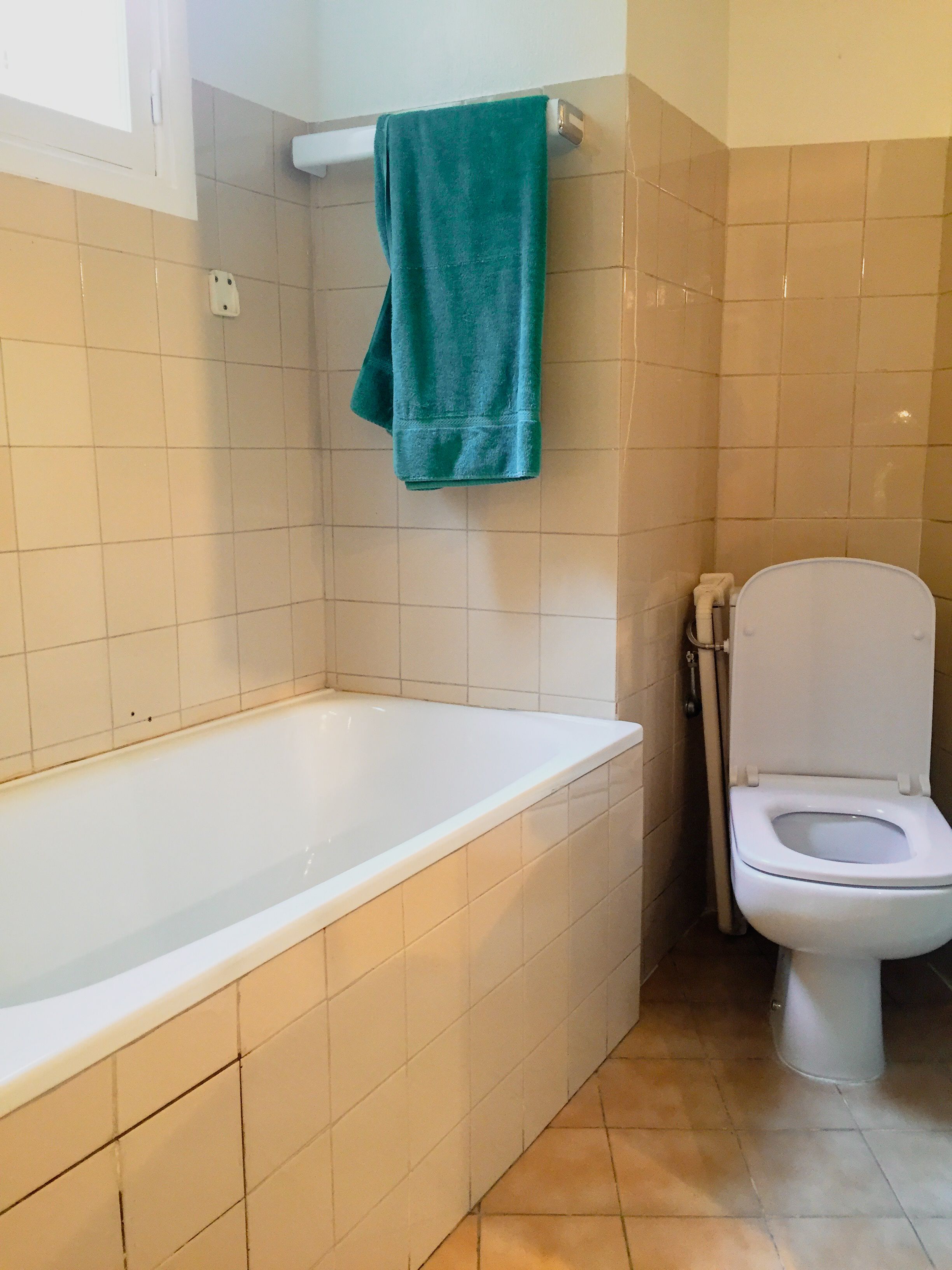 A bathroom with a white bathtub, a white toilet, and beige tiled walls.