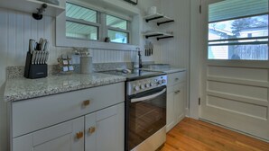 A kitchen with white cabinetry, a granite countertop, a stainless steel stove, and a window above the sink. - Lovely Brick Cottage in Downtown Blue Ridge (Blue Ridge)
