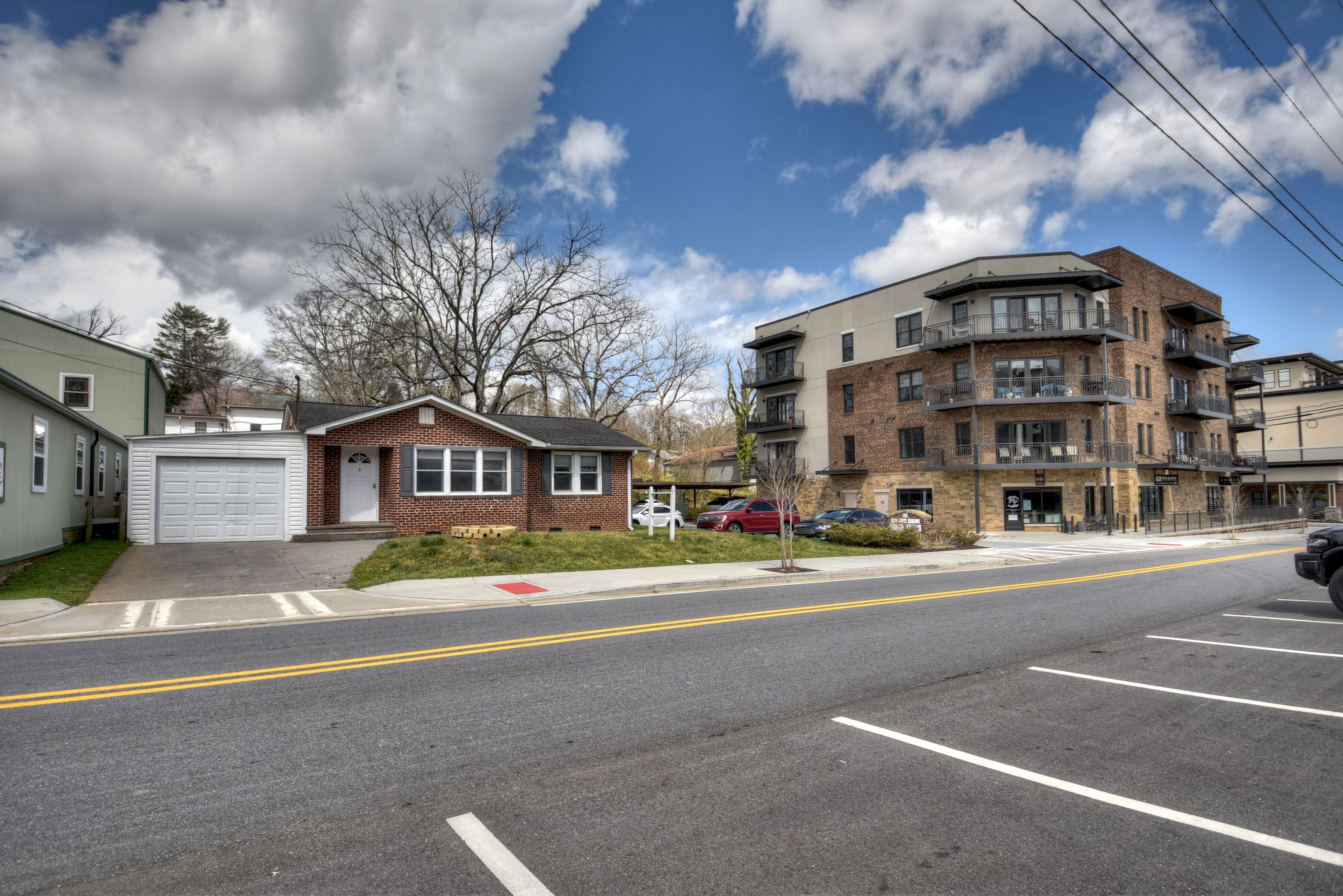 A street view with a two-story brick building with balconies, a small brick house, and a green building with a garage.