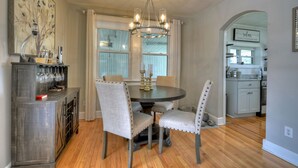 A dining area with a round table, four upholstered chairs, a chandelier, and a kitchen in the background. - Lovely Brick Cottage in Downtown Blue Ridge (Blue Ridge)