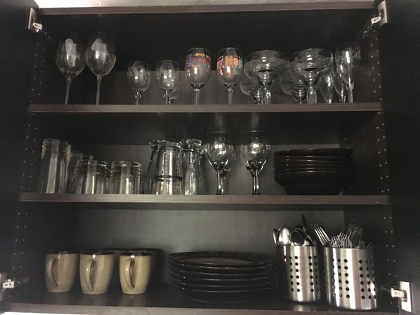 Une étagère de cuisine contenant divers articles en verre, notamment des verres à vin et des verres à cocktail, ainsi qu’un porte-ustensiles avec des cuillères et des fourchettes.