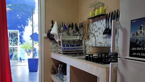 A kitchen with a tiled backsplash, a stove, and a refrigerator. There is a window with a view of a blue house and a tree outside.