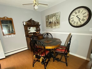 A dining room with a wooden table and chairs, a large wall clock, and a painting of a horse.