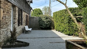 Un patio con camino de grava, un banco, un árbol pequeño y un muro de piedra.