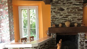 Una chimenea de piedra con repisa de madera, una pared de piedra y una ventana con vistas a la vegetación.