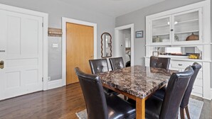 Un comedor con una mesa de mármol, sillas de cuero, una puerta de madera y un armario blanco con puertas de cristal.