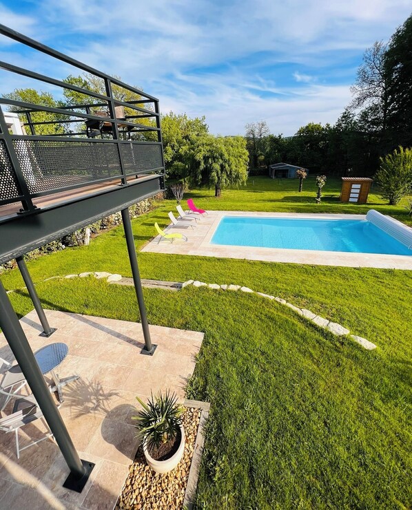 Un patio trasero con piscina, zona de estar cubierta y un pequeño jardín.
