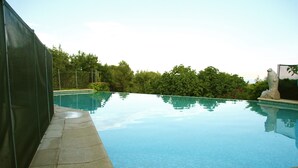 Ein Schwimmbecken mit klarem Wasser, umgeben von einer Steindeck und einem grünen Zaun.