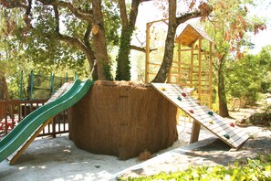 Une aire de jeux avec un toboggan, un mur d’escalade et une cabane en bois.