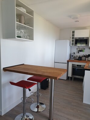 A modern kitchen with a wooden table, red bar stools, white cabinets, and stainless steel appliances.