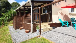 Ein überdachter Außenbereich mit Holzdeck, einer kleinen Sitzecke mit Stühlen und einem Blumentopf.