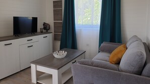 Ein modernes Wohnzimmer mit Flachbildfernseher, Couchtisch, Sofa und einem fenster mit Vorhängen.