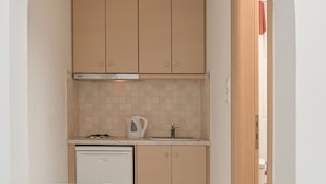 Une cuisine compacte avec des meubles en bois, un plan de travail blanc, un petit lave-vaisselle et un pare-feu en carrelage.