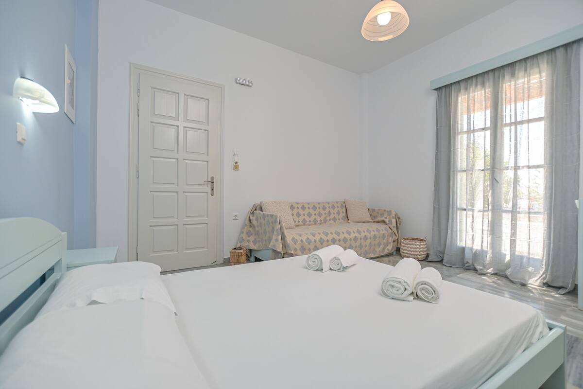 Una habitación de hotel con cama, sofá, ventana con cortinas y puerta.