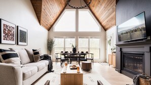 Ein gemütliches Wohnzimmer mit hohen Decken, einem Kamin, einem Essbereich und einem Fernseher, der über dem Kamin befestigt ist.